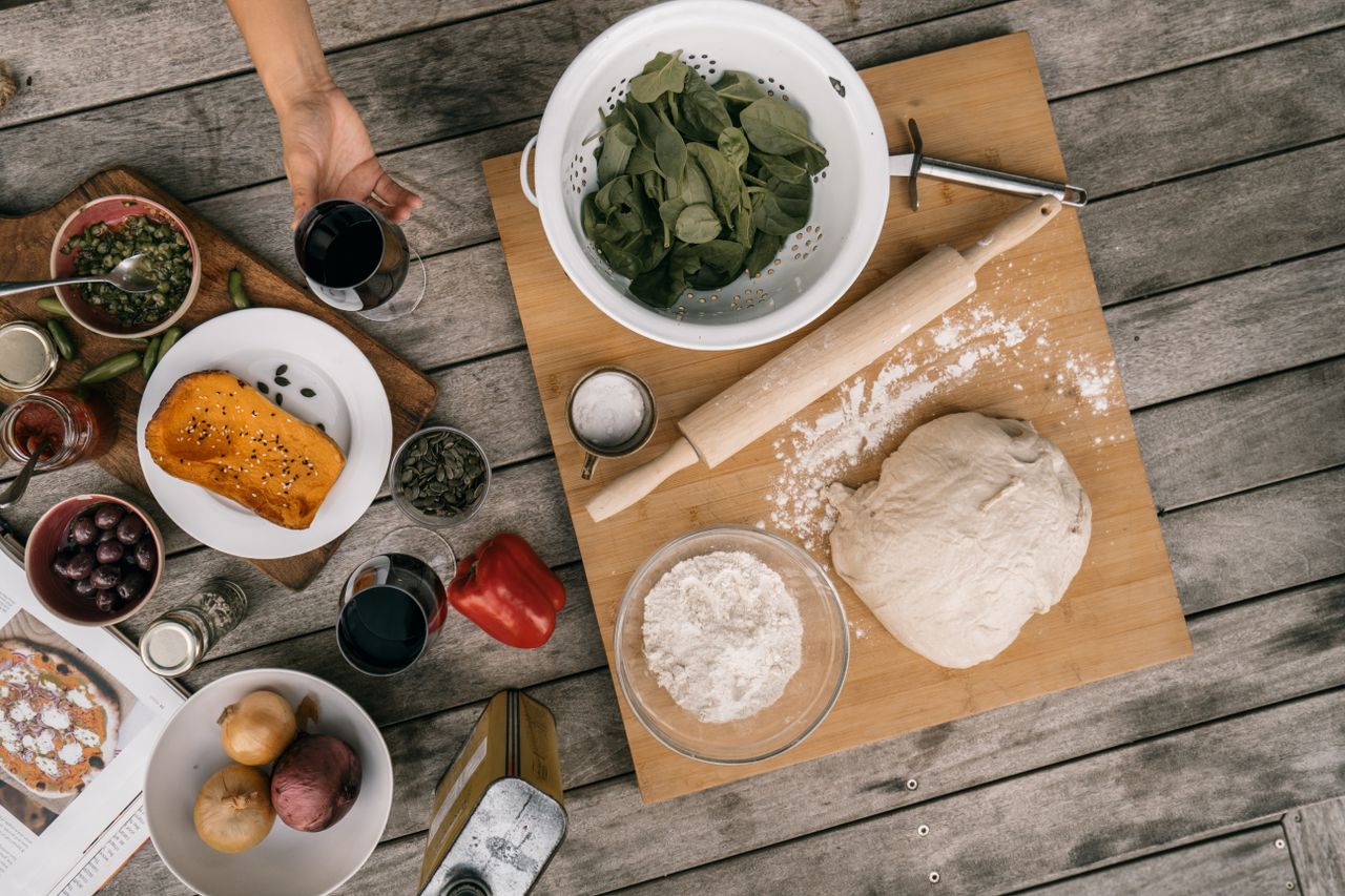 Home An overhead view of ingredients and tools for making homemade pizza on a wooden table.