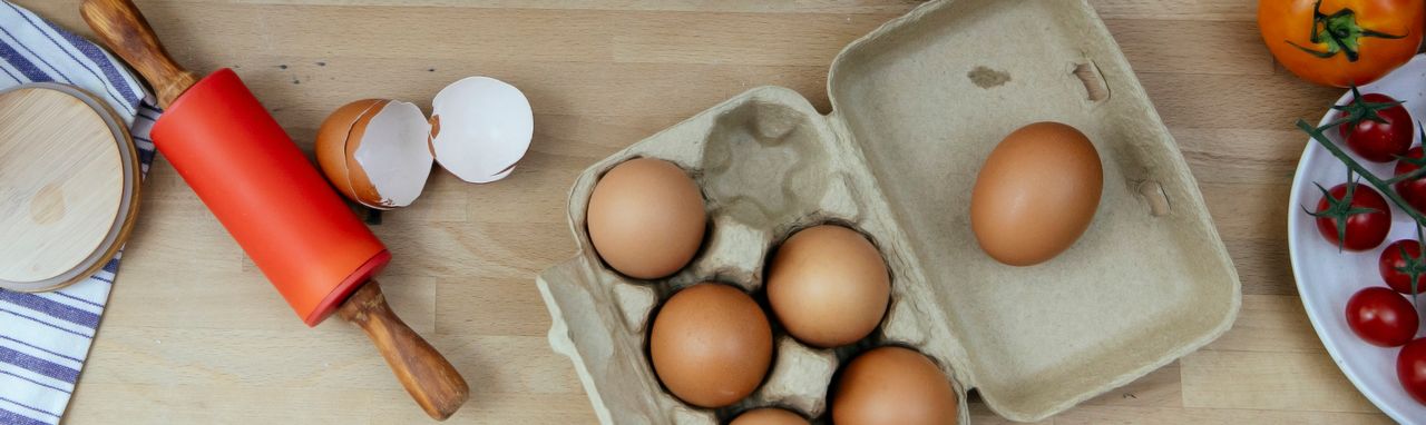 Top view of eggs and eggshell on wooden table with rolling pin and tomatoes placed in kitchen during cooking process